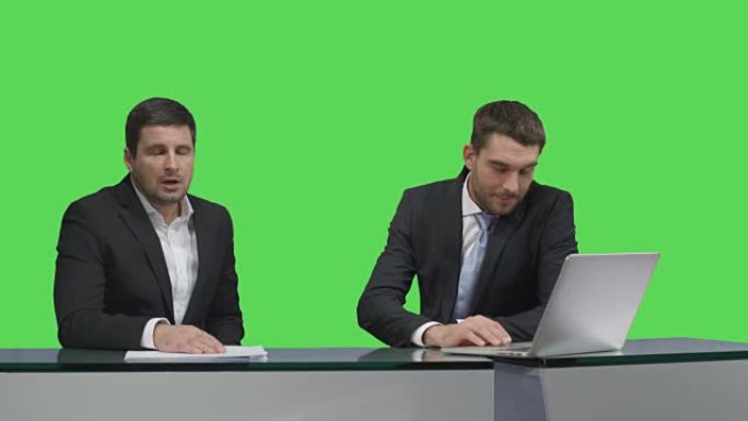两家媒体广播公司坐在一台笔记本电脑的桌子旁，在后台的模拟绿屏上聊天。