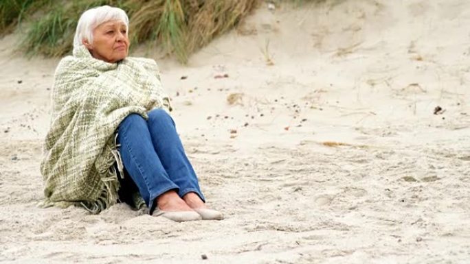 体贴的退休妇女坐在沙滩上