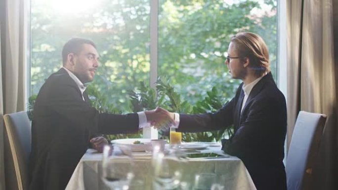 两名穿着西装的商人在一家餐馆进行了交谈，并与握手达成了协议。