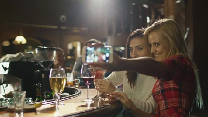 两个漂亮的女孩正在智能手机上自拍，同时在酒吧里玩得很开心。