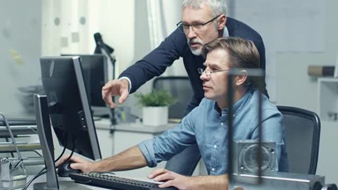 在繁忙的工程局中，两名高级工程师通过个人计算机讨论技术问题。他们的办公室看起来简约而现代。
