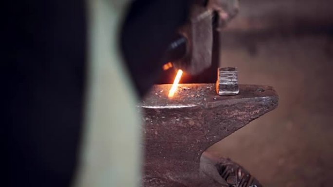 铁匠用锤子和热红色金属工作。两个男人在铁匠铺的铁砧上锻造铁