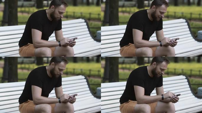 特写迷人的年轻人坐在公园的长椅上，使用智能手机