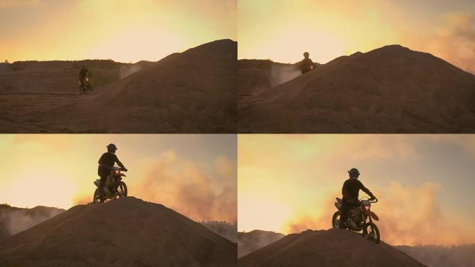 专业摩托车越野赛摩托车骑手驾驶越过沙丘和更远的越野轨道。这是《日落》，赛道上布满了烟雾。