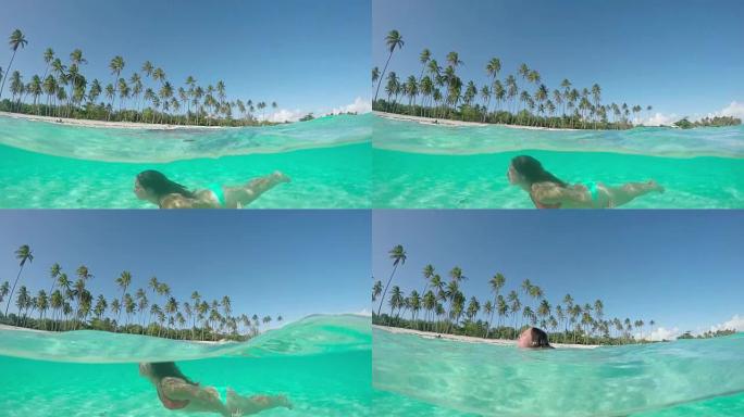4k慢动作半水下特写: 穿着比基尼的快乐年轻女子暑假在异国情调的法属波利尼西亚的热带岛屿上水下游泳