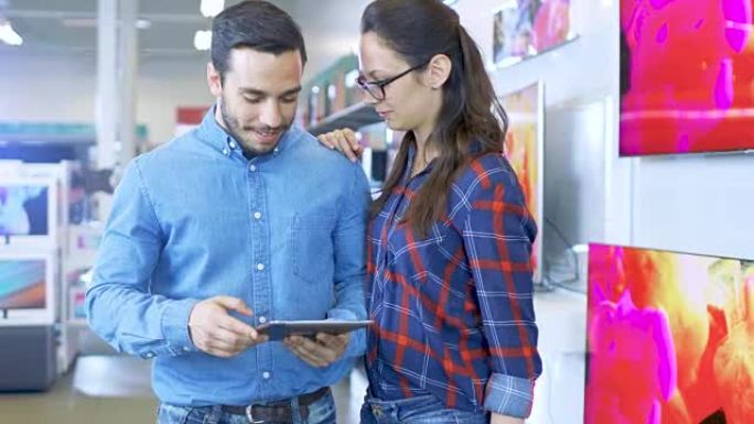 电子商店里的年轻美丽夫妇正在寻找最新的平板电脑型号，为他们的使用和预算选择合适的型号。商店明亮而现代