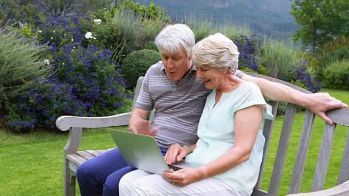 高级夫妇在长凳上交谈和使用笔记本电脑