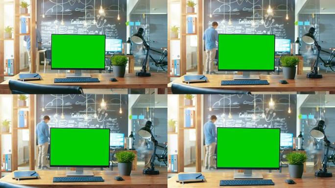 带有模拟绿屏监视器的个人计算机站在办公桌上，背景是白天在创意办公室工作的人。