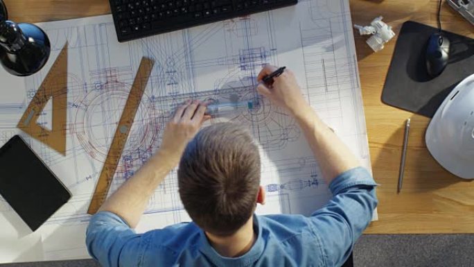 一位技术工程师在绘制蓝图，利用计划的俯视图。各种各样的绘画对象躺在他的桌子上。