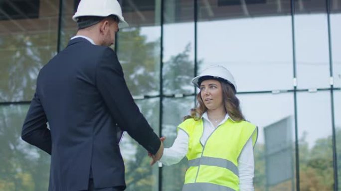 戴安全帽的商人和女工程师在建筑工地上握手协议。
