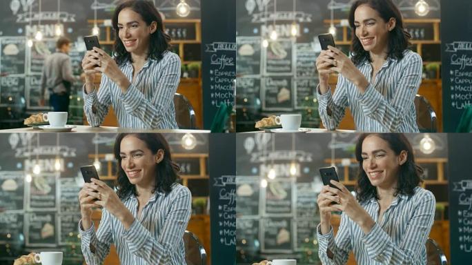 美丽的女人坐在咖啡馆里使用智能手机。她在给朋友或爱人发消息时微笑。在她端着饮料和羊角面包的桌上杯子上