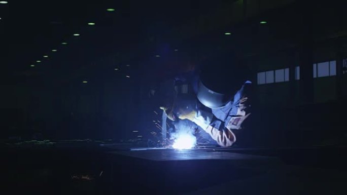 一家工厂的重工业工人正在黑暗的内部焊接金属。