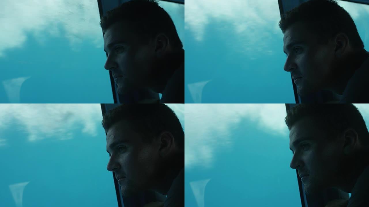 一个男人在玻璃底部的船上看着水下生活的特写镜头。