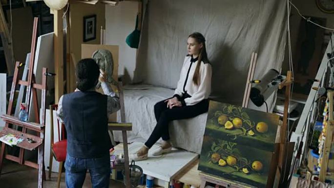 雕塑家在画布上创作人脸雕塑，而年轻女子在艺术工作室对他摆姿势