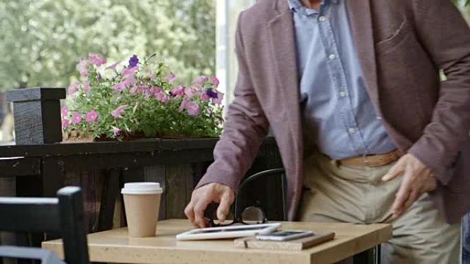 老年商人从咖啡馆的数字平板电脑上阅读