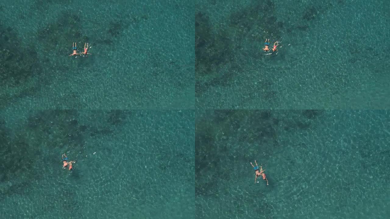 空中: 年轻夫妇在翡翠海洋中游泳并互相取笑