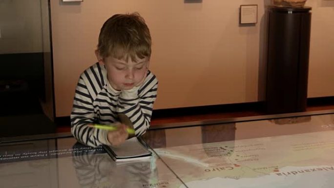 博物馆中的男孩研究地图并在R3D上拍摄的笔记本中写字