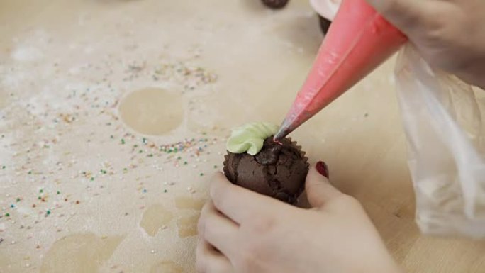 用彩色奶油装饰巧克力蛋糕的女性双手的特写视图，为此使用糕点袋