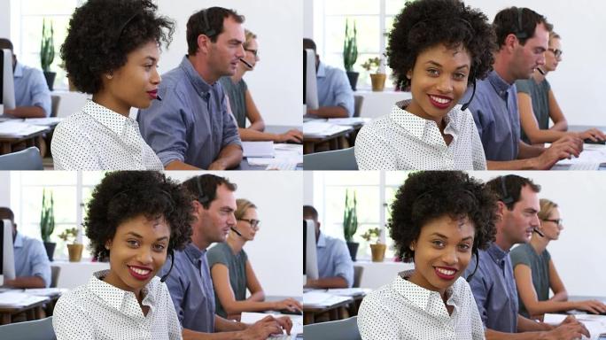 戴着耳机的黑人妇女在开放式办公室向相机微笑