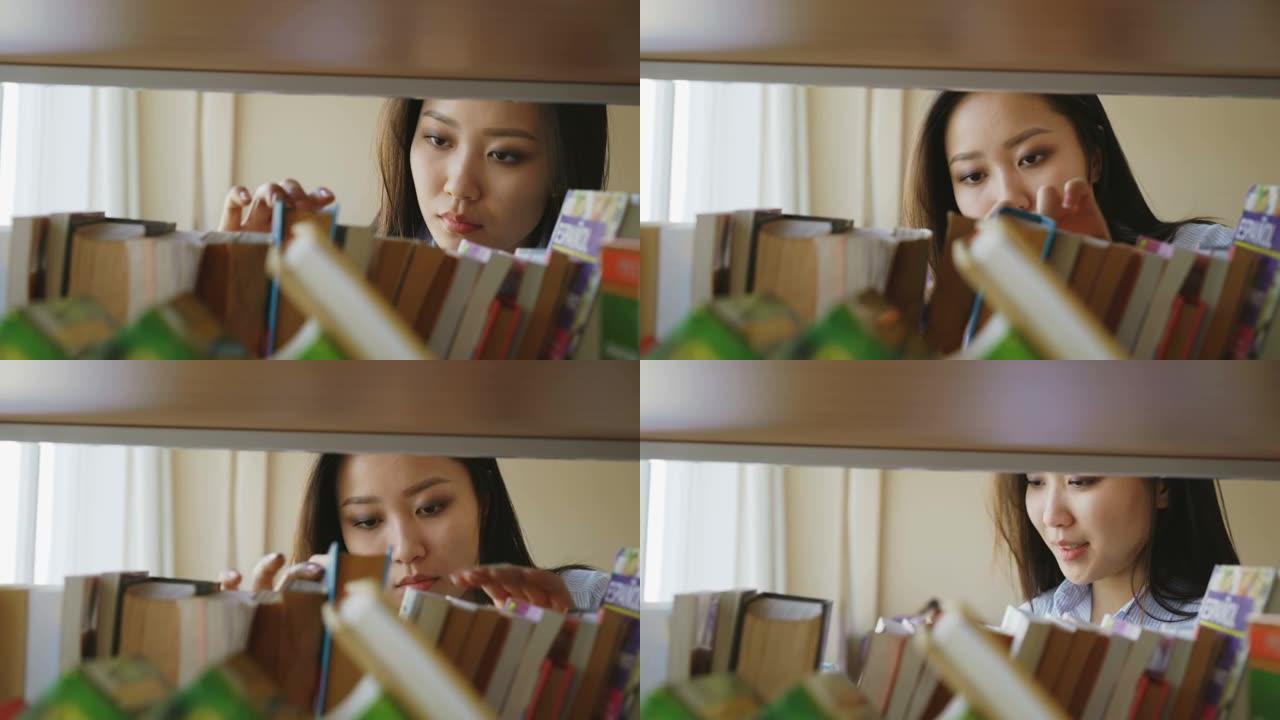 美丽的亚洲体贴的女学生在大图书馆的书架上寻找必要的书，打开一本书，微笑着满意