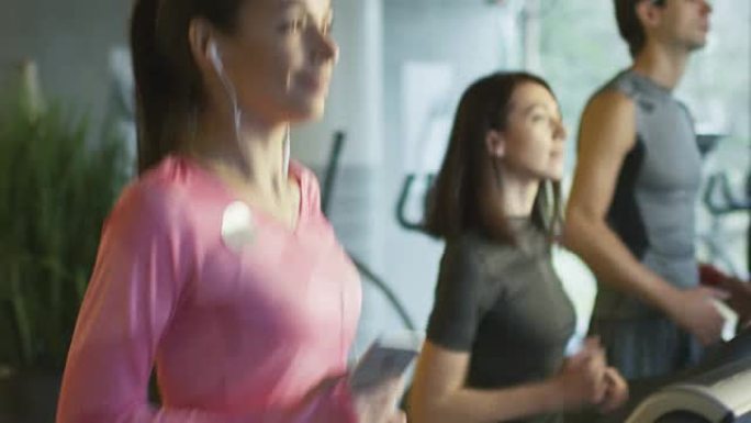 有吸引力的高加索女孩在运动健身房用耳机在跑步机上跑步的慢动作镜头。