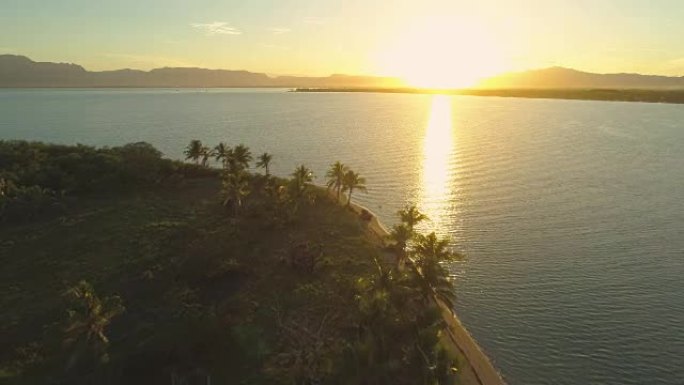 空中: 日出时在宁静的热带岛屿的空旷沙滩上飞行。