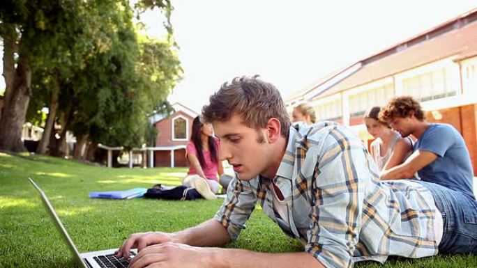 学生与坐在草地后面的同学一起使用笔记本电脑