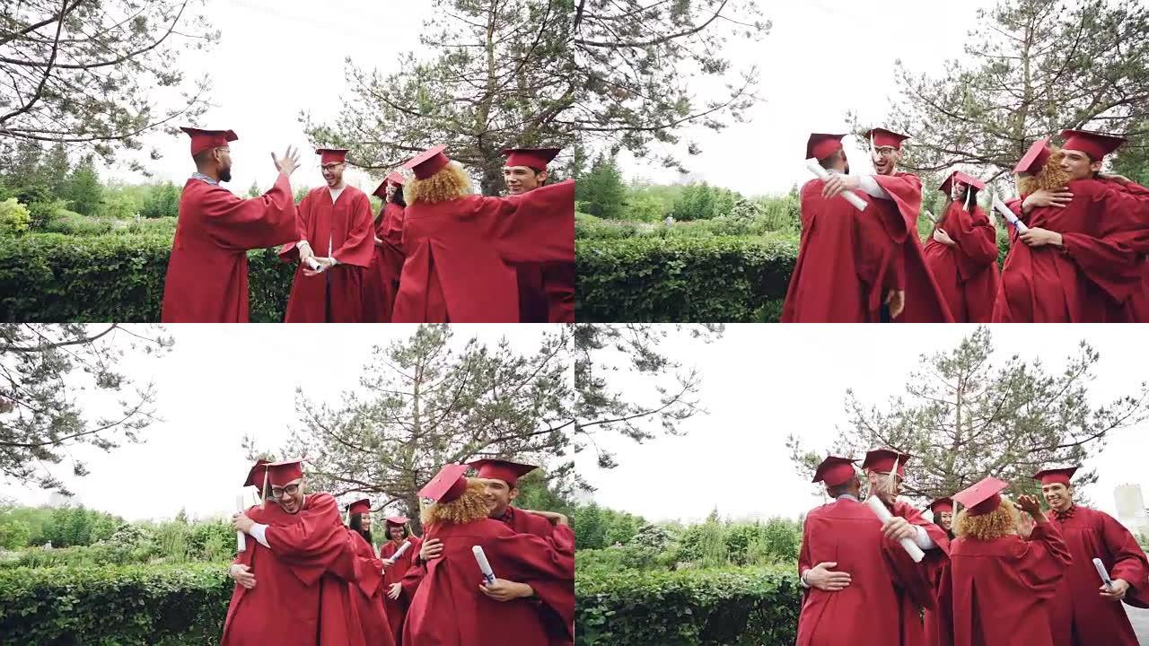 朋友的慢动作即将毕业的学生高五岁，互相拥抱，戴着砂浆板帽和长袍，拿着文凭。校园、事件和人的概念。