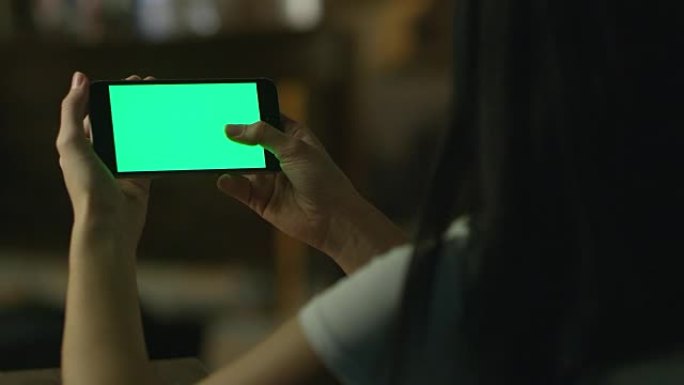 十几岁的女孩在晚上在风景模式下使用带有绿屏的智能手机。休闲生活方式。