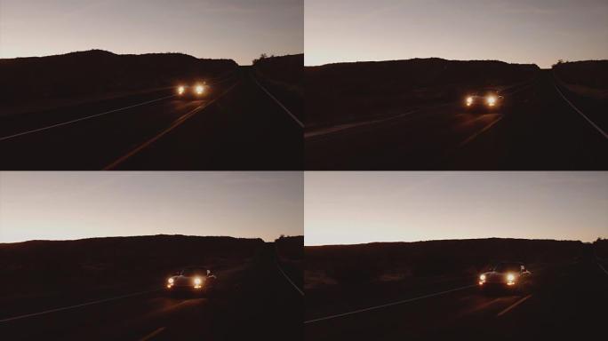 鸟瞰图红色经典汽车在黄昏时沿着荒凉的沙漠路行驶，前灯开着