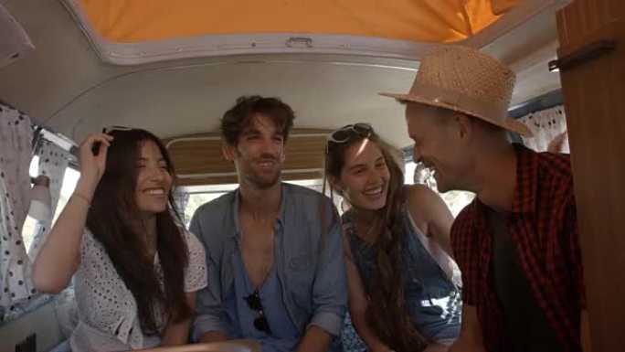 公路旅行中的四个朋友在露营车的后面聊天