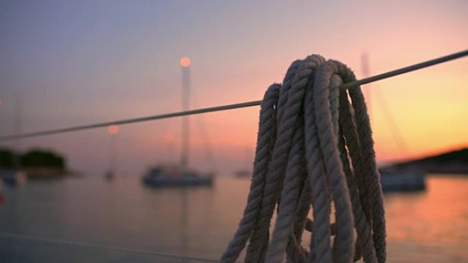 4k绳子挂在栏杆上，俯瞰帆船停泊在宁静的日落海洋上，实时