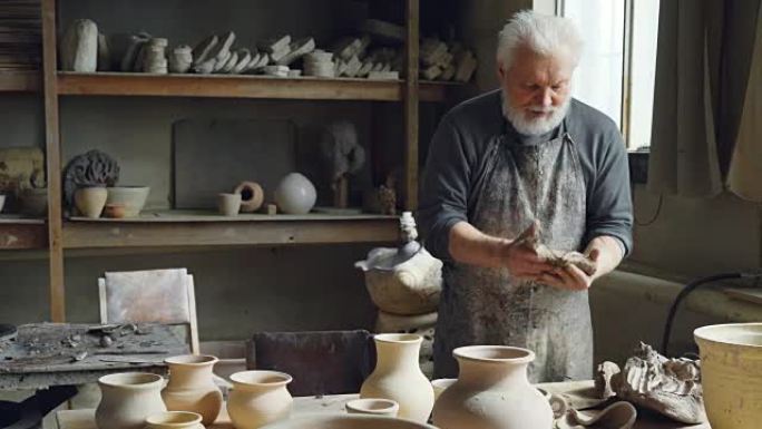 专业的男陶艺家正在用陶工的设备，工具和许多陶瓷人物在小作坊里揉捏粘土，形成粘土球。