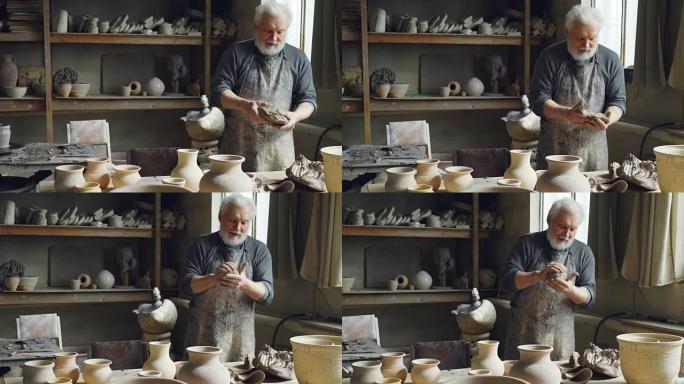 专业的男陶艺家正在用陶工的设备，工具和许多陶瓷人物在小作坊里揉捏粘土，形成粘土球。