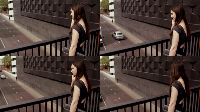 性感的女商人使用智能手机站在俯瞰道路的桥上，steadicam拍摄。慢mo