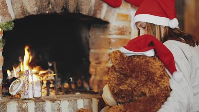 4k女孩和戴着圣诞老人帽子的泰迪熊在圣诞壁炉旁放松，实时