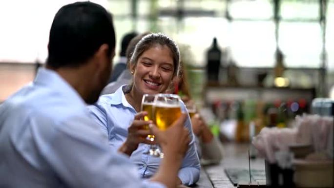 酒吧里的年轻夫妇享受着啤酒，在欢乐时光里敬酒