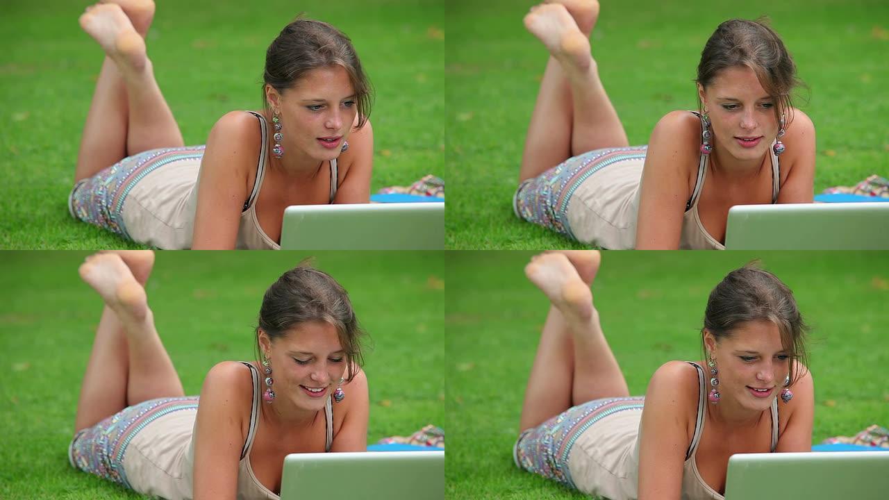 快乐的学生躺在草地上使用笔记本电脑