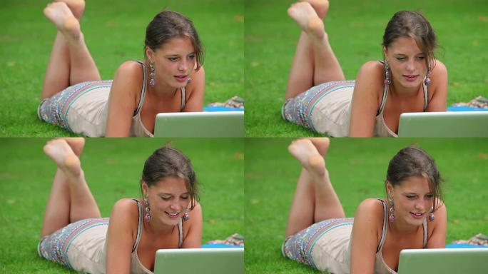 快乐的学生躺在草地上使用笔记本电脑