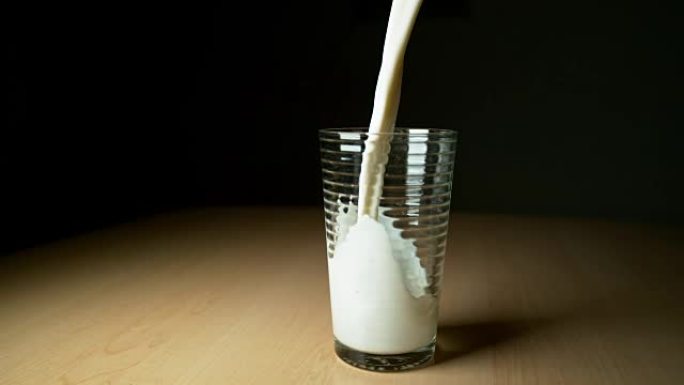 超级慢动作美味的冷牛奶倒在木制桌子上的空玻璃杯中