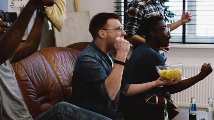 非裔美国朋友在电视上观看体育节目。慢动作。球迷们用爆米花在沙发上兴奋地庆祝进球。情感
