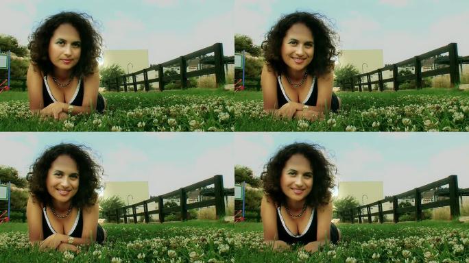年轻的皮肤黝黑、面带微笑的女人躺在草坪上