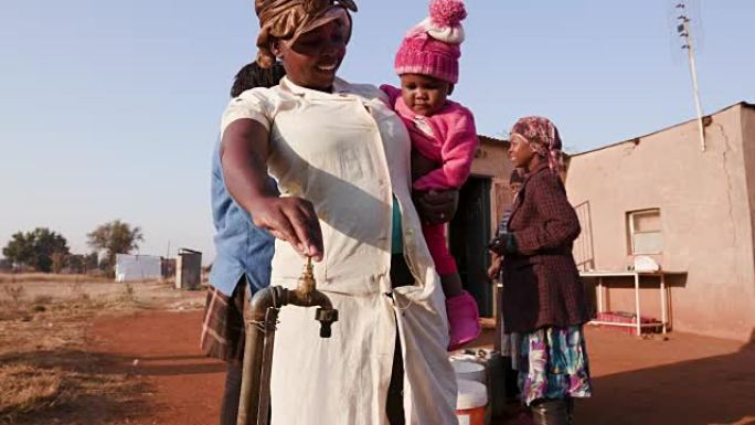 非洲妇女在装满一桶水时与婴儿交谈