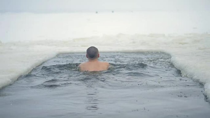 降雪时，一个人在冰冻的河里游泳。