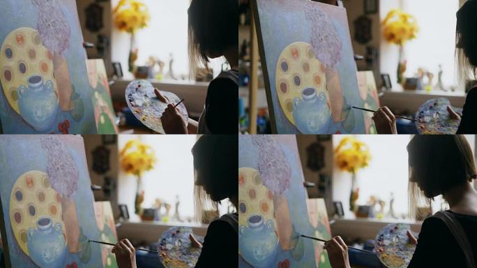 年轻艺术家女人的特写在画室把画笔和画笔混合在调色板上，在画布上画静物画