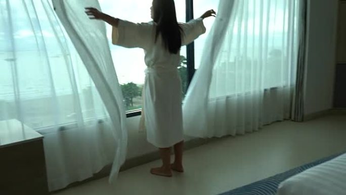 4k镜头亚洲妇女早晨醒来，在豪华酒店卧室的床上散步和看着窗户，生活方式和休闲概念