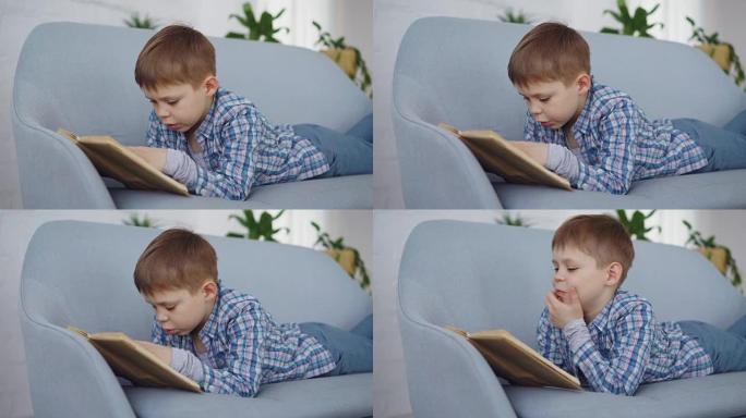 穿着休闲服的可爱小男孩正躺在舒适的沙发上大声朗读有趣的书。快乐童年、学前教育和爱好概念。