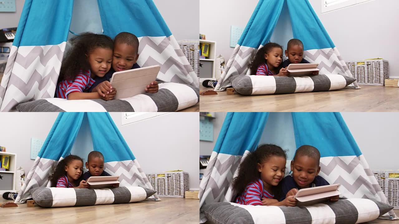 两个孩子躺在带数字平板电脑的游戏室的帐篷里