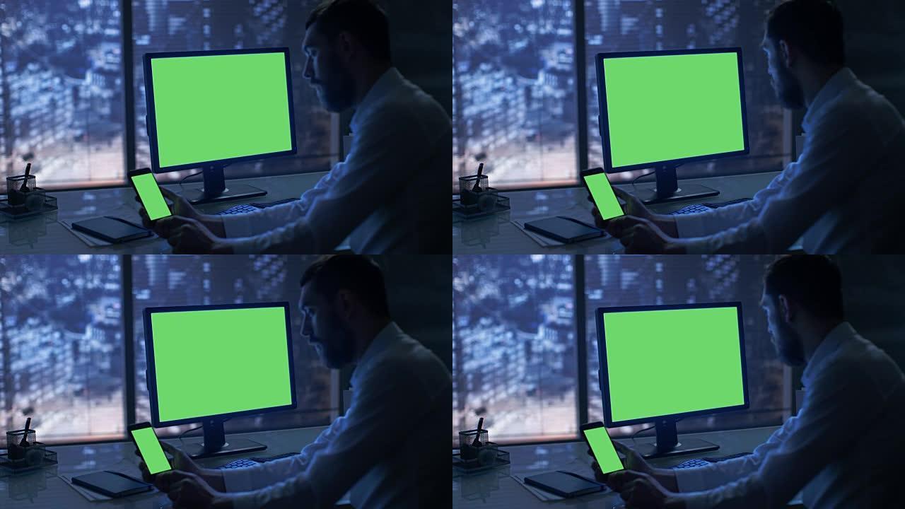 深夜商人在他的私人办公室里用绿色模拟屏幕的个人电脑和智能手机工作，可以看到大城市的窗户。