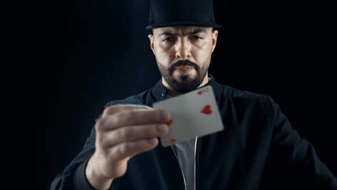 戴着帽子的专业街头魔术师多次执行卡片消失和外观技巧。背景是黑色的。